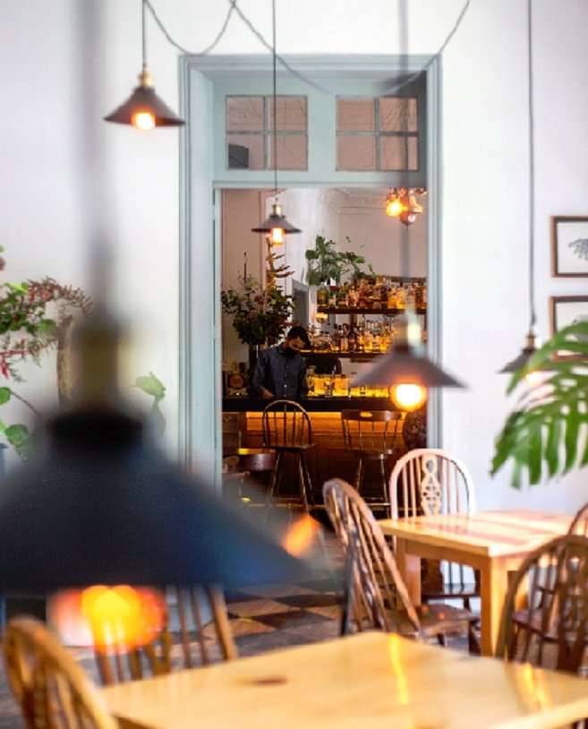 Salón de la casona con mesas de madera, lámparas y vista a la barra