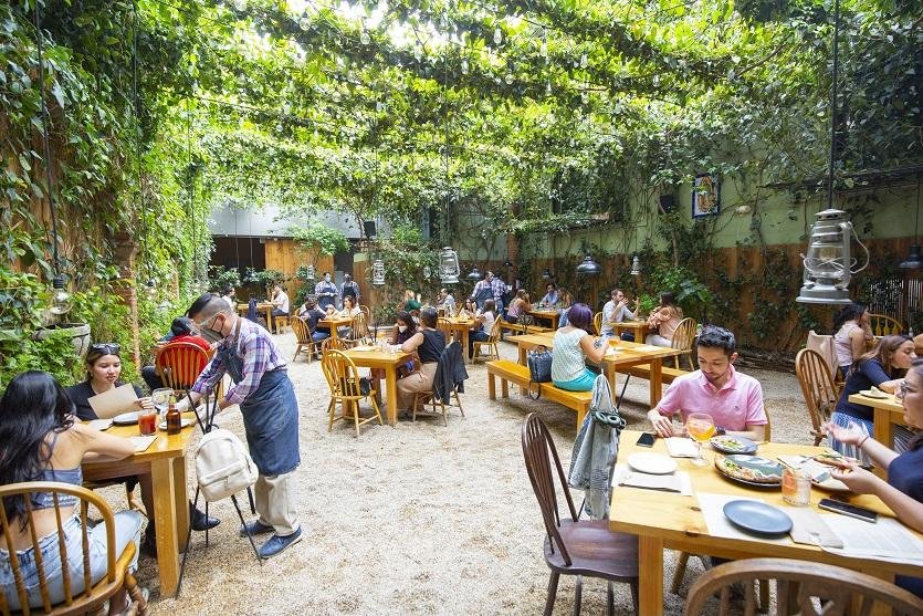 Patio de grava rodeado de vegetación con mesas ocupadas